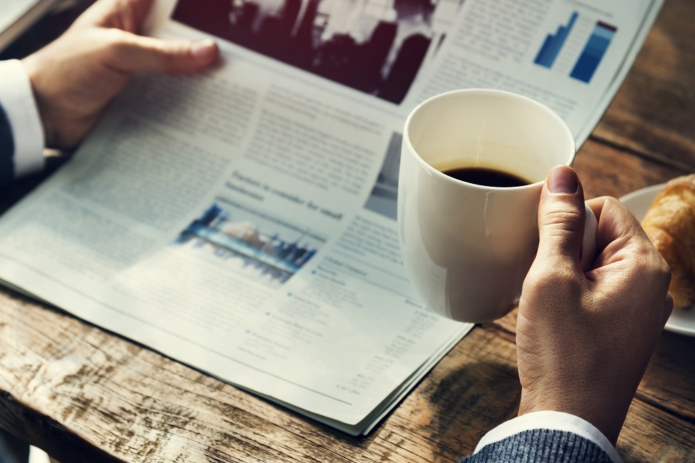 A businessman reading newspaper while holding a cup of coffee